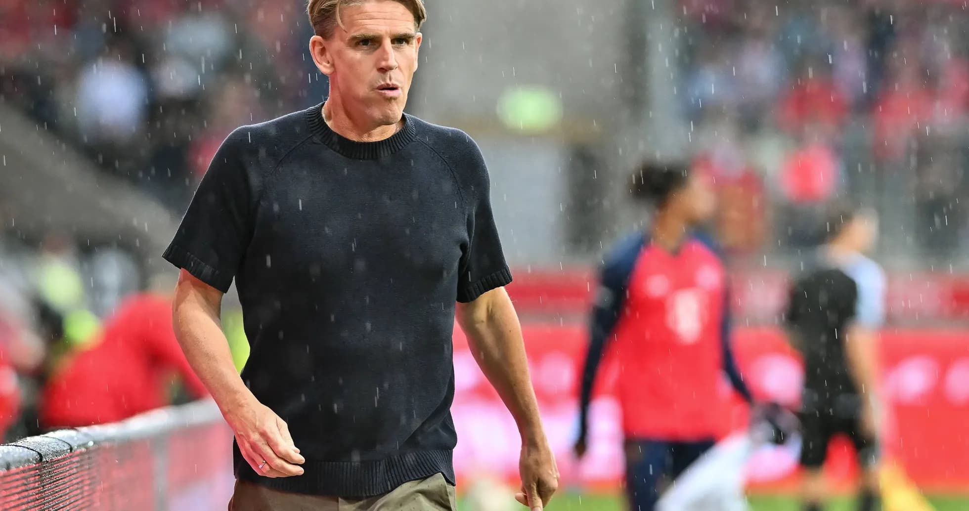 Entrenador caminando en campo bajo la lluvia
