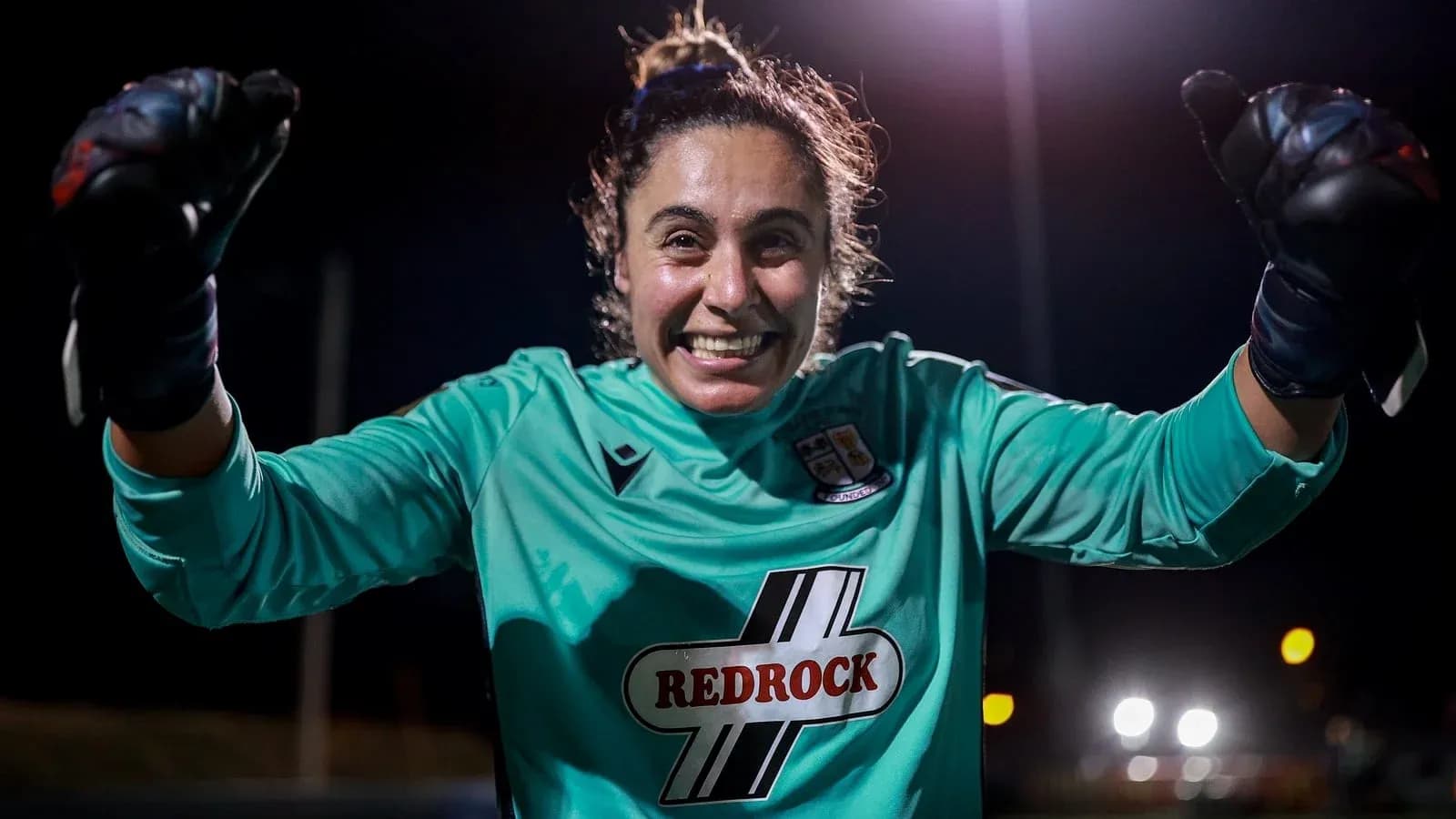 Portera celebrando con guantes en campo iluminado
