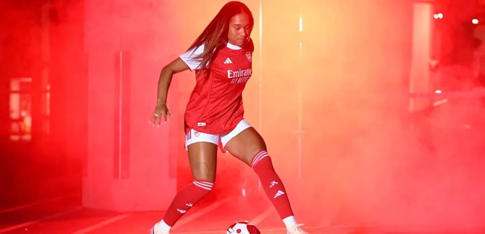 Jugadora de fútbol con balón en fondo de humo rojo
