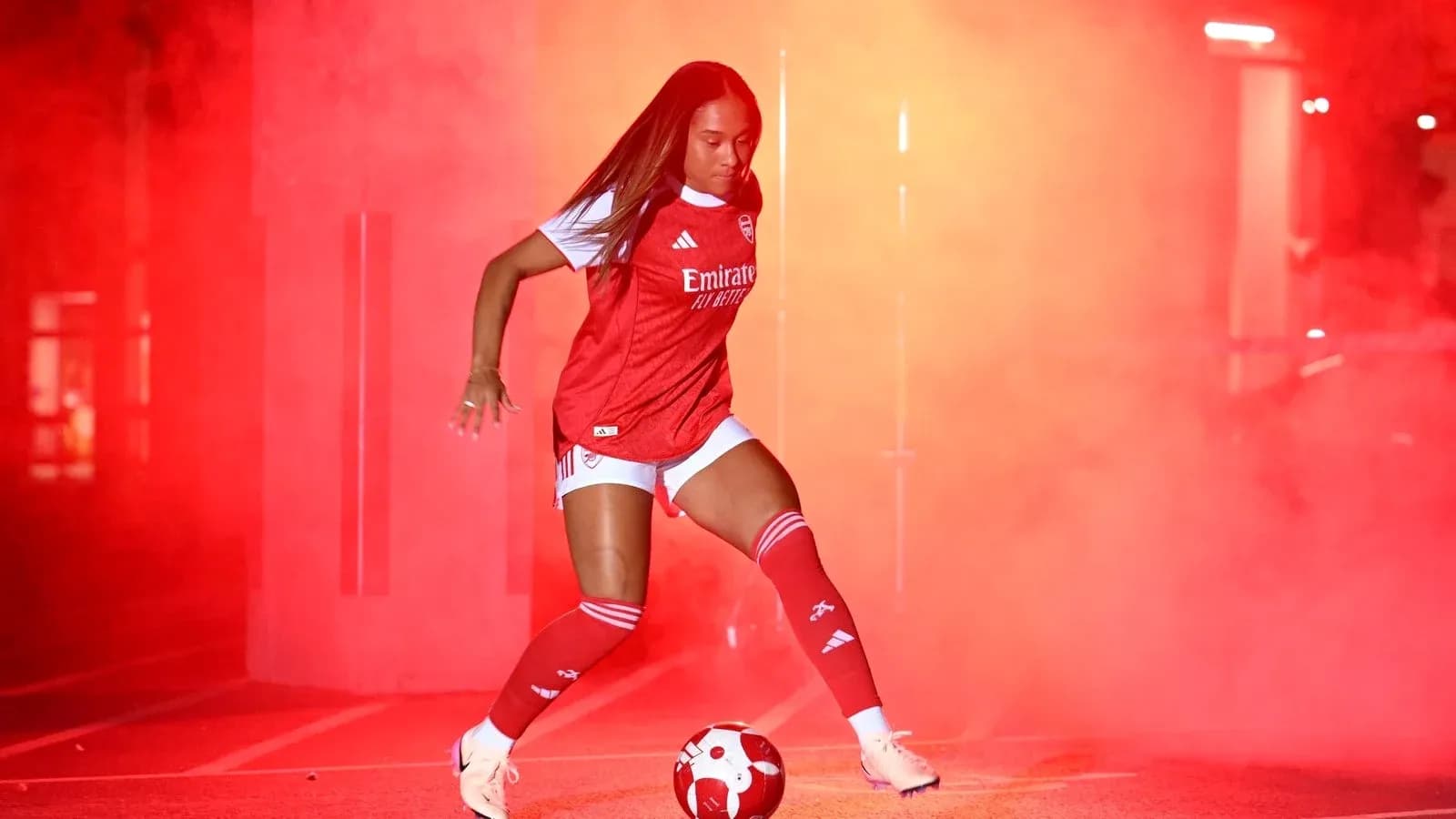 Jugadora de fútbol con balón en fondo de humo rojo