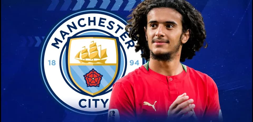 Jugador de fútbol con camiseta roja frente al logo de Manchester City