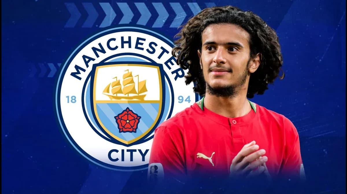 Jugador de fútbol con camiseta roja frente al logo de Manchester City