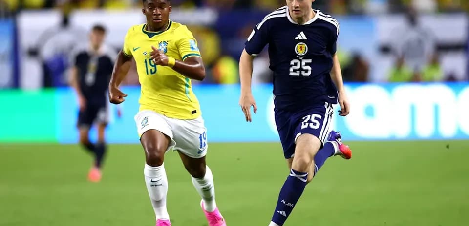 Jugador de Escocia corriendo con balón, seguido por jugador brasileño