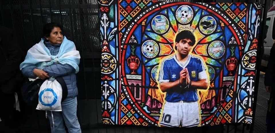 Mujer con bandera argentina junto a mural de Maradona