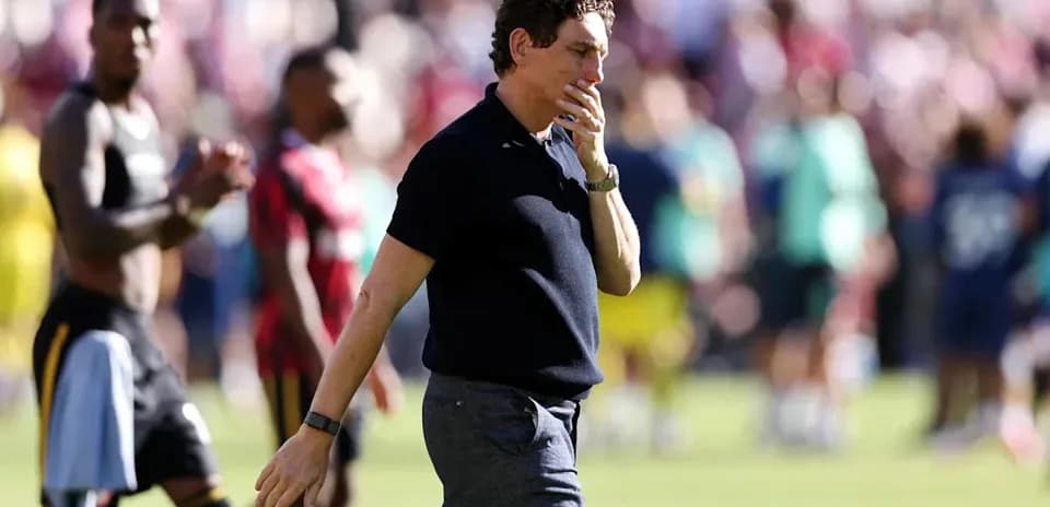 Entrenador caminando tras el partido con jugadores de fondo