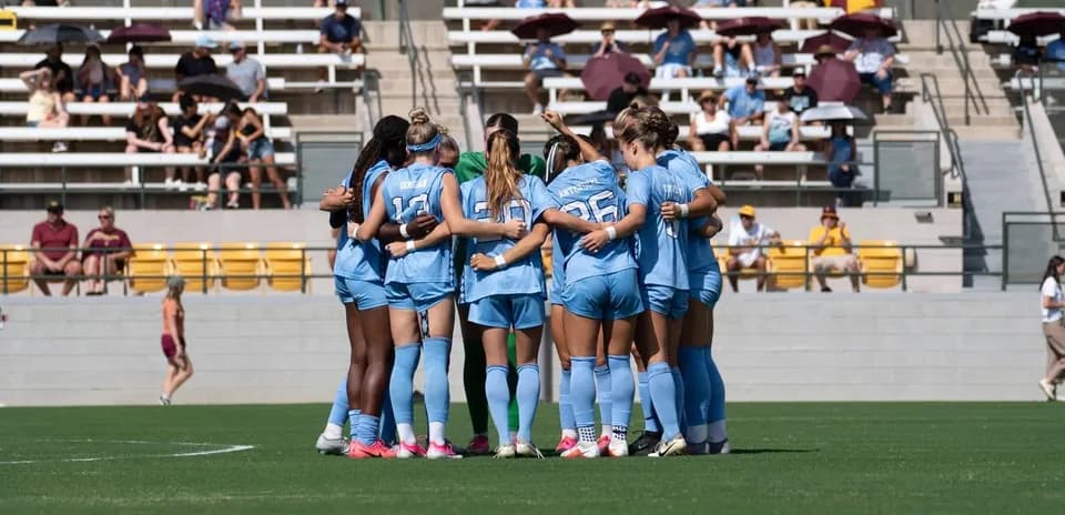 Equipo femenino de fútbol formando un círculo en el campo