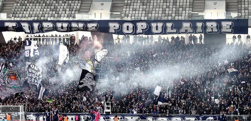 Aficionados animando en el estadio con humo y banderas