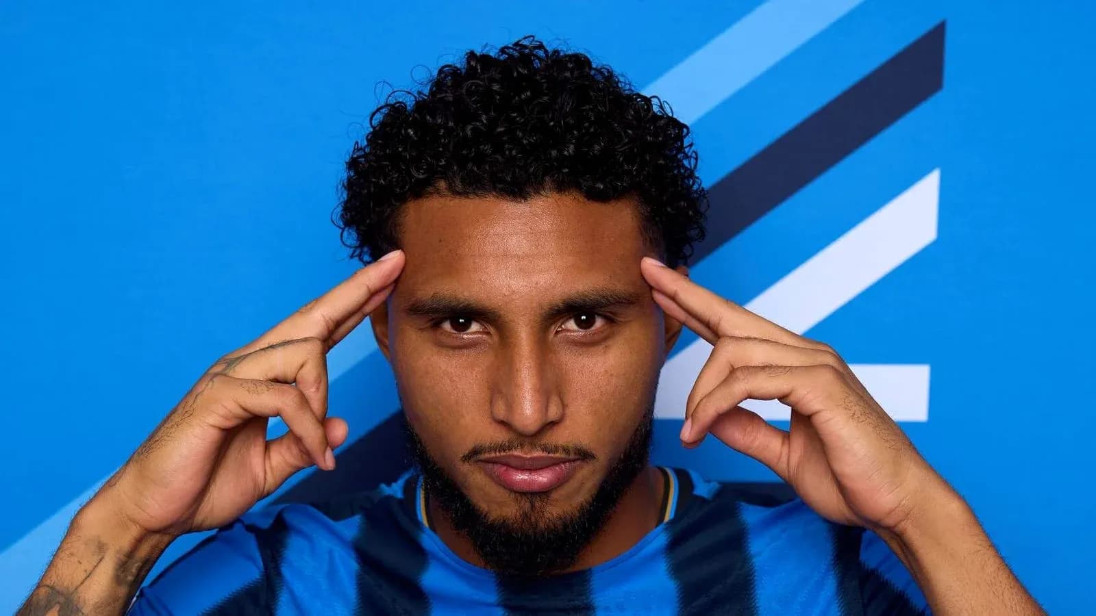 Jugador posando con fondo azul y gesto pensativo Jugador posando con fondo azul y gesto pensativo