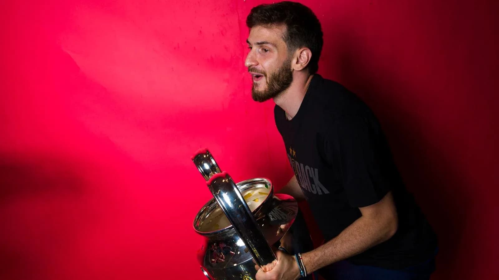 Jugador sosteniendo un trofeo frente a fondo rojo Jugador sosteniendo un trofeo frente a fondo rojo